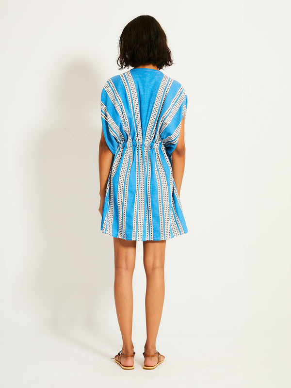 Back of a Woman Standing Wearing lemlem ALEM Dress featuring classic Amira pattern with small geometric bands that float on a rich teal blue ground