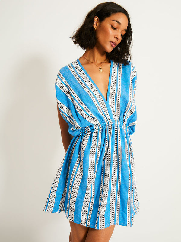 Woman Standing Wearing lemlem ALEM Dress featuring classic Amira pattern with small geometric bands that float on a rich teal blue ground