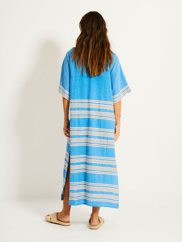 Back of a Woman Standing Wearing lemlem EDNA Dress featuring classic Amira pattern with small geometric bands that float on a rich teal blue ground