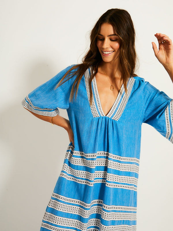 Woman Standing Wearing lemlem EDNA Dress featuring classic Amira pattern with small geometric bands that float on a rich teal blue ground