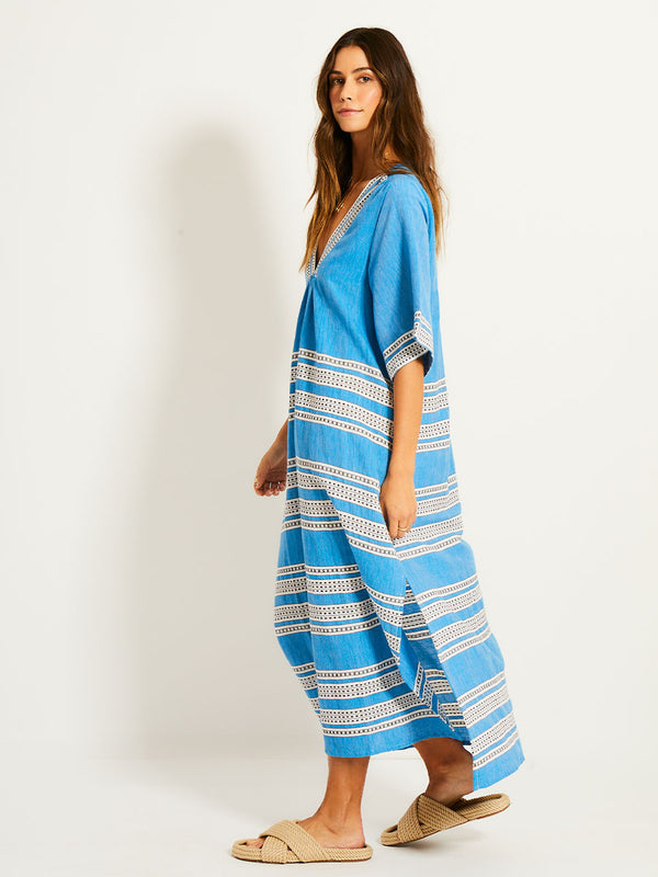 Side Shot of a Woman Standing Wearing lemlem EDNA Dress featuring classic Amira pattern with small geometric bands that float on a rich teal blue ground