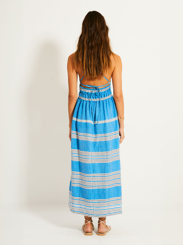 Back of a Woman Standing Wearing lemlem GETE Dress featuring classic Amira pattern with small geometric bands that float on a rich teal blue ground