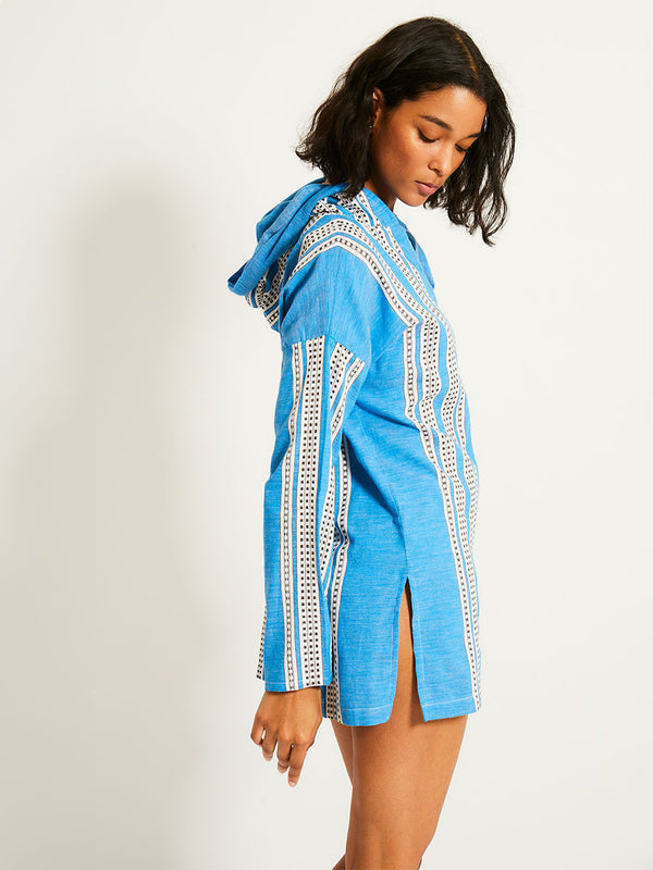 Side shot of a Woman Standing Wearing lemlem HENOK Hoodie featuring classic Amira pattern with small geometric bands that float on a rich teal blue ground