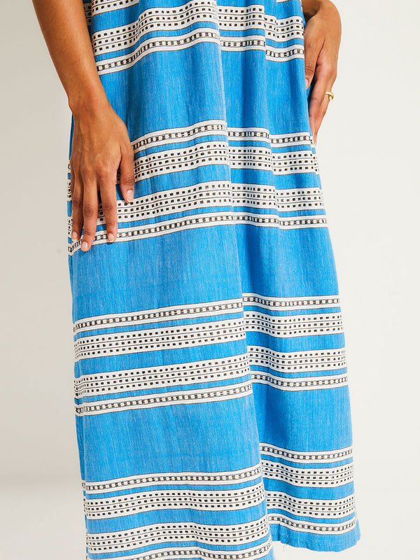 Close up on a Woman Standing Wearing lemlem  MELAT Dress featuring classic Amira pattern with small geometric bands that float on a rich teal blue ground and classic one piece swimsuit in teal color