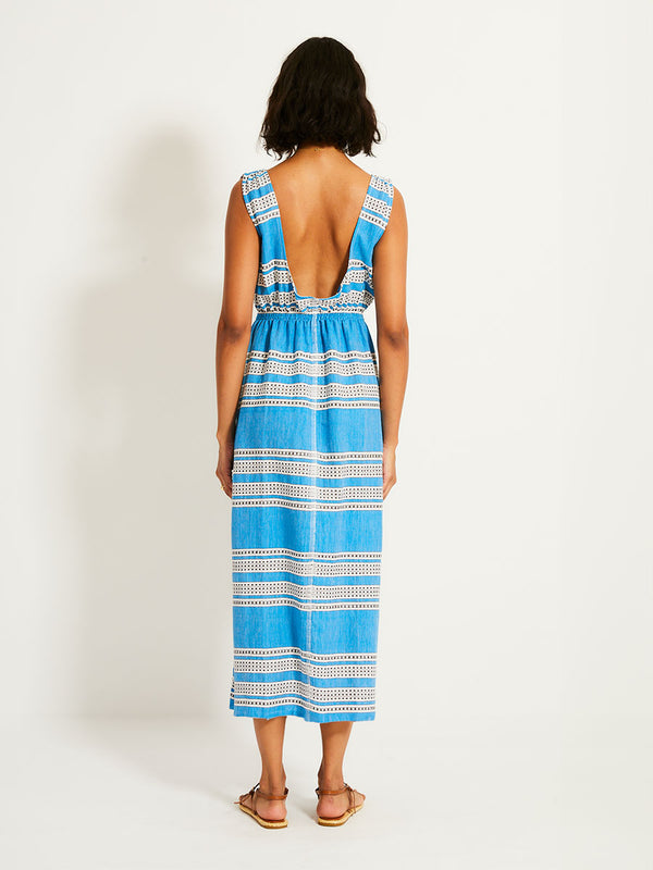 Back of a Woman Standing Wearing lemlem  MELAT Dress featuring classic Amira pattern with small geometric bands that float on a rich teal blue ground and classic one piece swimsuit in teal color