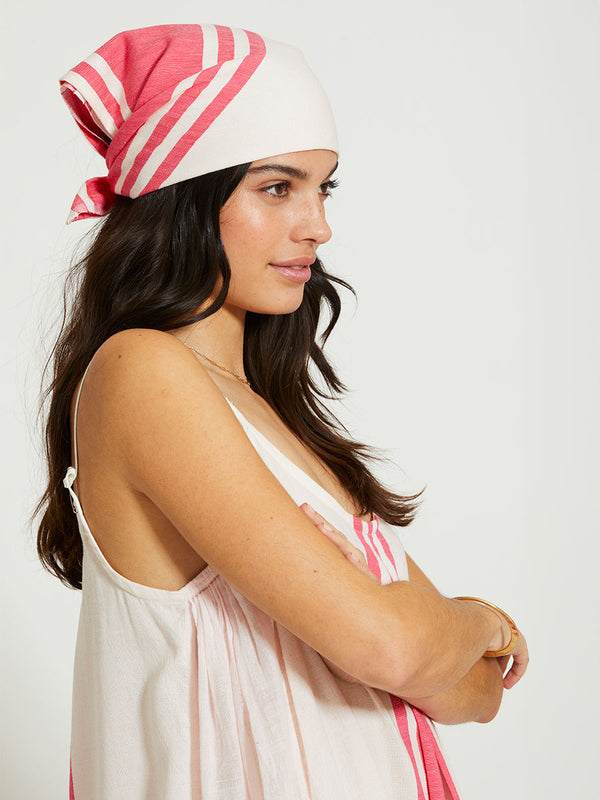 Side shot of Woman Standing Wearing lemlem DANA | Bandana featuring bold two-tone stripe pattern in watermelon pink and soft rosy cream