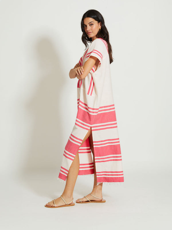 Side shot of a Woman Standing Wearing lemlem GASIRA | V Neck Caftan featuring bold two-tone stripe pattern in watermelon pink and soft rosy cream