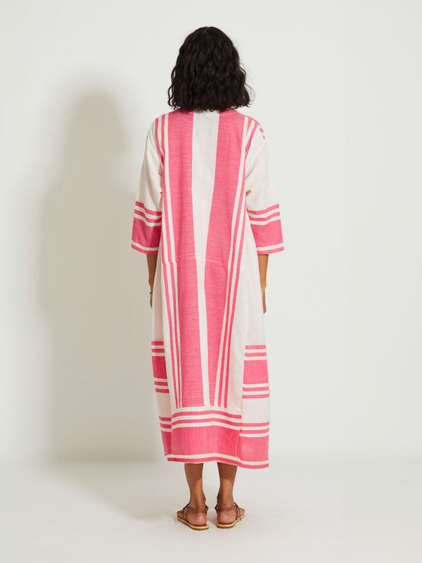 Back of a Woman Standing Wearing lemlem FANA | Caftan featuring bold two-tone stripe pattern in watermelon pink and soft rosy cream