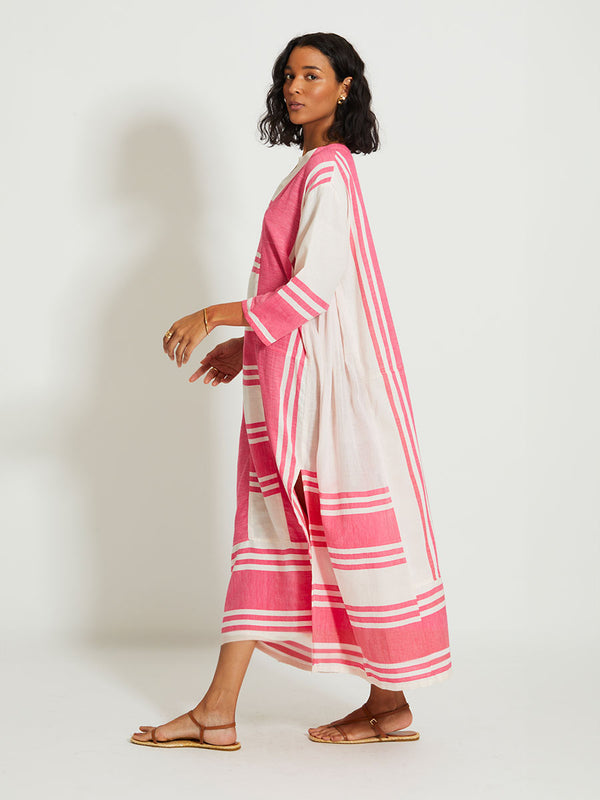 Woman Walking Wearing lemlem FANA | Caftan featuring bold two-tone stripe pattern in watermelon pink and soft rosy cream