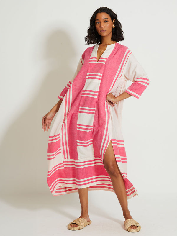 Woman Standing Wearing lemlem FANA | Caftan featuring bold two-tone stripe pattern in watermelon pink and soft rosy cream