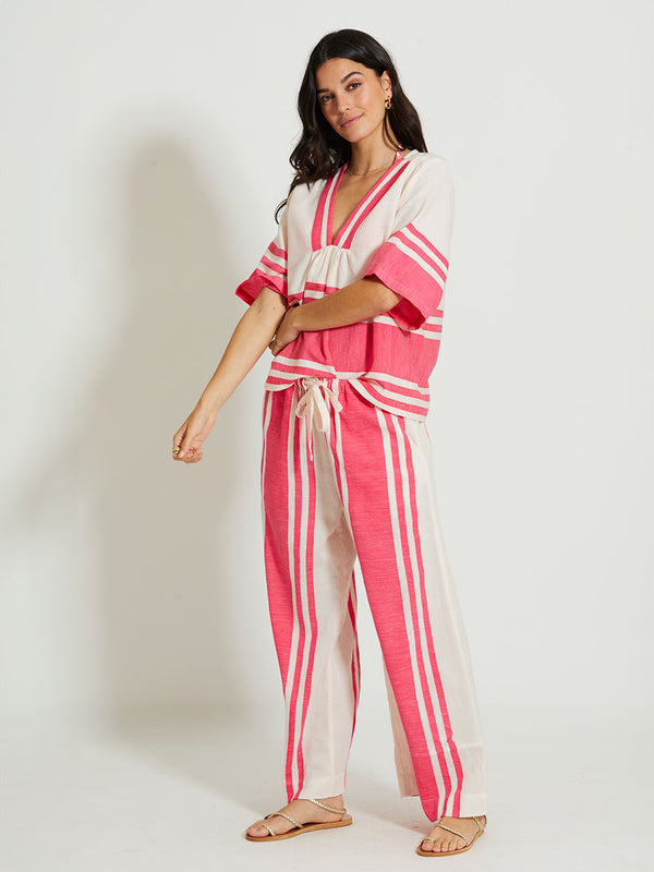 Woman Standing Wearing lemlem RITA | V Neck Top featuring bold two-tone stripe pattern in watermelon pink and soft rosy cream and matching pants