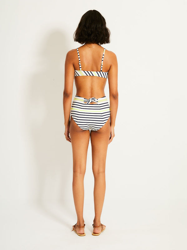 Back of a Woman Standing Wearing lemlem ELSI High Waist Bottom featuring an ivory ground with navy stripes, accented by khaki and citron hues
