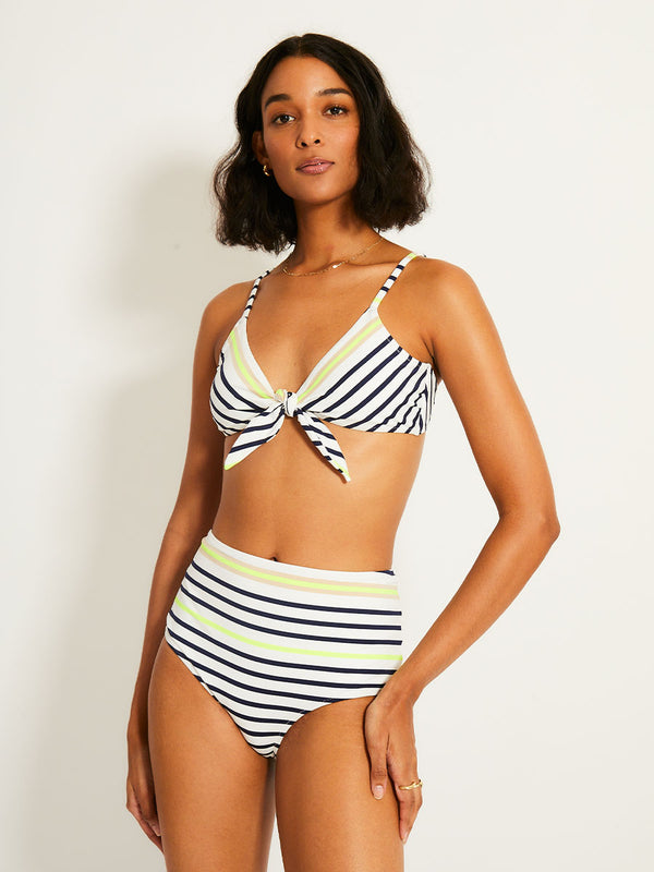 Woman Standing Wearing lemlem SARA Tie Front Top featuring an ivory ground with navy stripes, accented by khaki and citron hues

