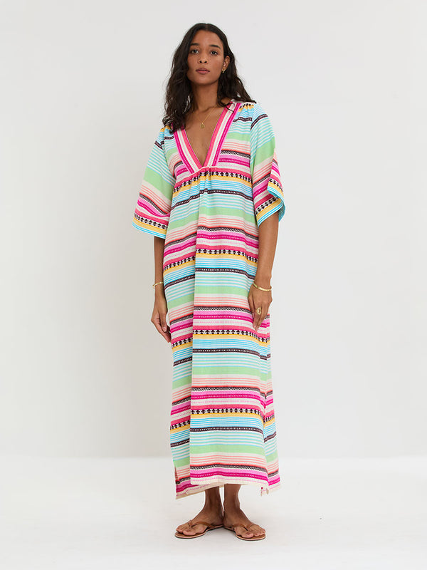 Woman Standing Wearing lemlem handwoven EDNA Dress featuring intricate stripes and a tibeb pattern in vivid combinations of green, aqua, turquoise, pink, and soft peach-tangerine tones.
