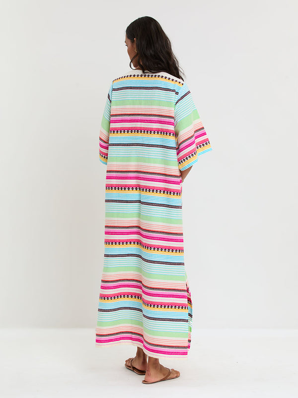 Back of a Woman Standing Wearing lemlem handwoven EDNA Dress featuring intricate stripes and a tibeb pattern in vivid combinations of green, aqua, turquoise, pink, and soft peach-tangerine tones.