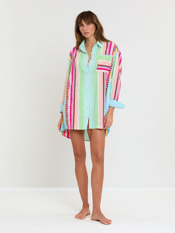 Woman Standing Wearing lemlem handwoven MARIAM Shirt featuring intricate stripes and a tibeb pattern in vivid combinations of green, aqua, turquoise, pink, and soft peach-tangerine tones.