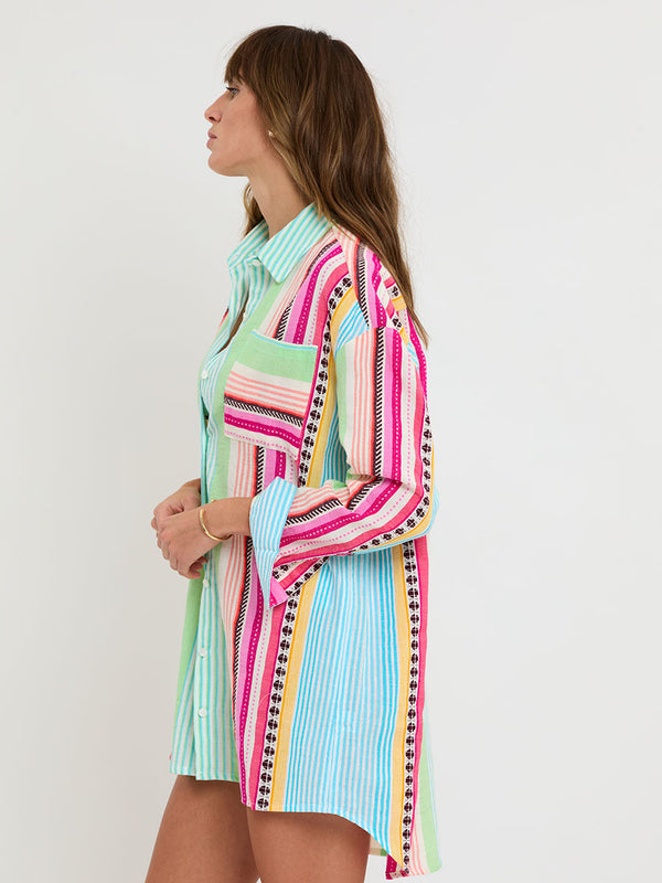 Woman Standing Wearing lemlem handwoven MARIAM Shirt featuring intricate stripes and a tibeb pattern in vivid combinations of green, aqua, turquoise, pink, and soft peach-tangerine tones.