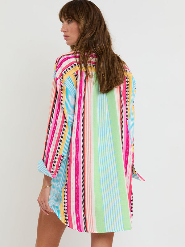 Woman Standing Wearing lemlem handwoven MARIAM Shirt featuring intricate stripes and a tibeb pattern in vivid combinations of green, aqua, turquoise, pink, and soft peach-tangerine tones.