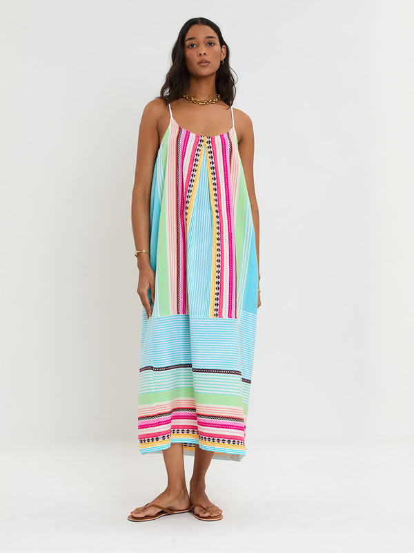 Woman Standing Wearing lemlem handwoven NIA Dress featuring intricate stripes and a tibeb pattern in vivid combinations of green, aqua, turquoise, pink, and soft peach-tangerine tones.