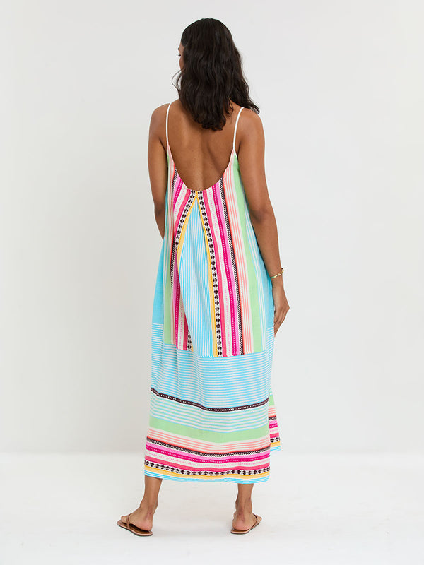 Woman Standing Wearing lemlem handwoven NIA Dress featuring intricate stripes and a tibeb pattern in vivid combinations of green, aqua, turquoise, pink, and soft peach-tangerine tones.
