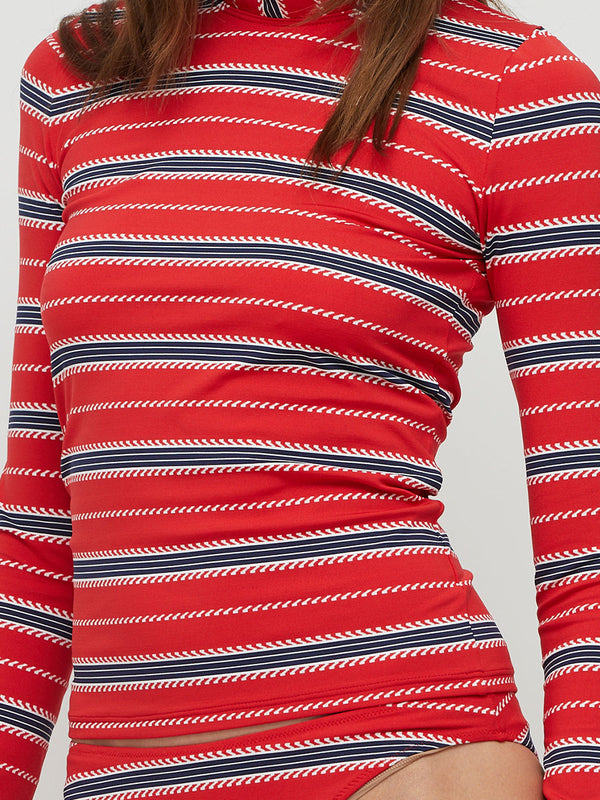  woman standing wearing lemlem AZEB Rashguard featuring stripe pattern in navy and white on bright red background