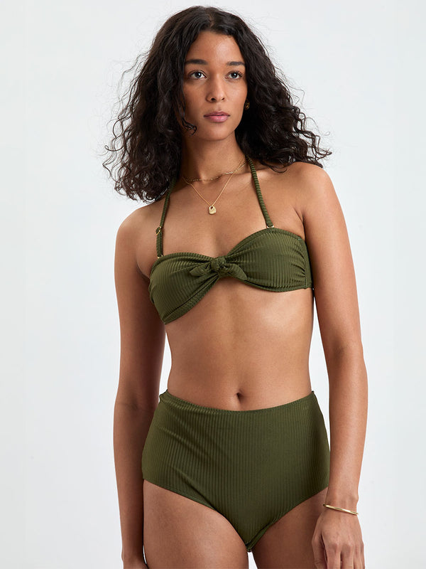 Close up on a Woman wearing lemlem ELSI High Waist Bottom and AVA Bandeau Bikini Top featuring a rich olive green color and a soft, silky ribbed texture fabric