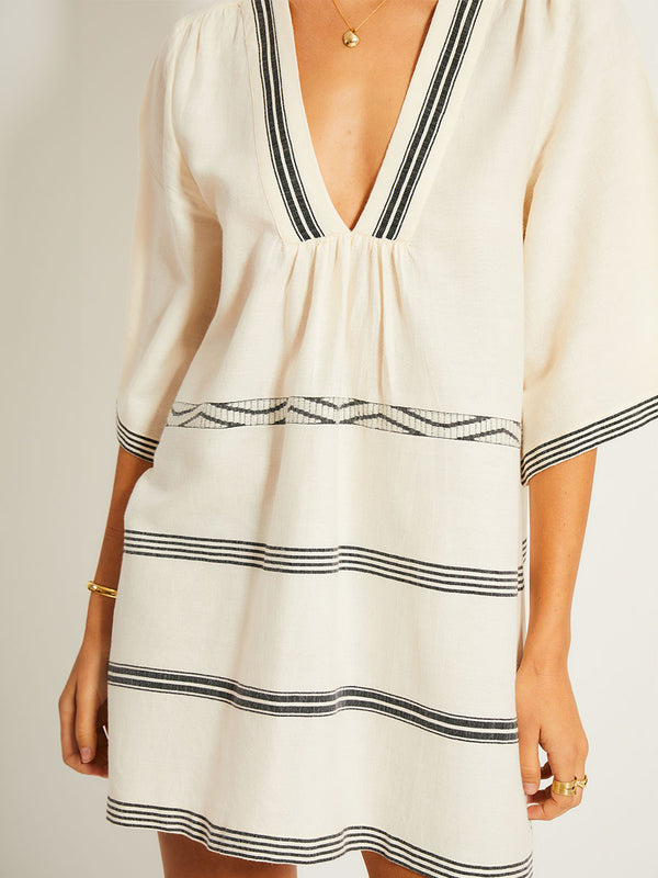 Close up on a Woman Standing Wearing lemlem BELKIS Caftan featuring  black intricate stripes and a Tibeb wave band on a soft vanilla ground