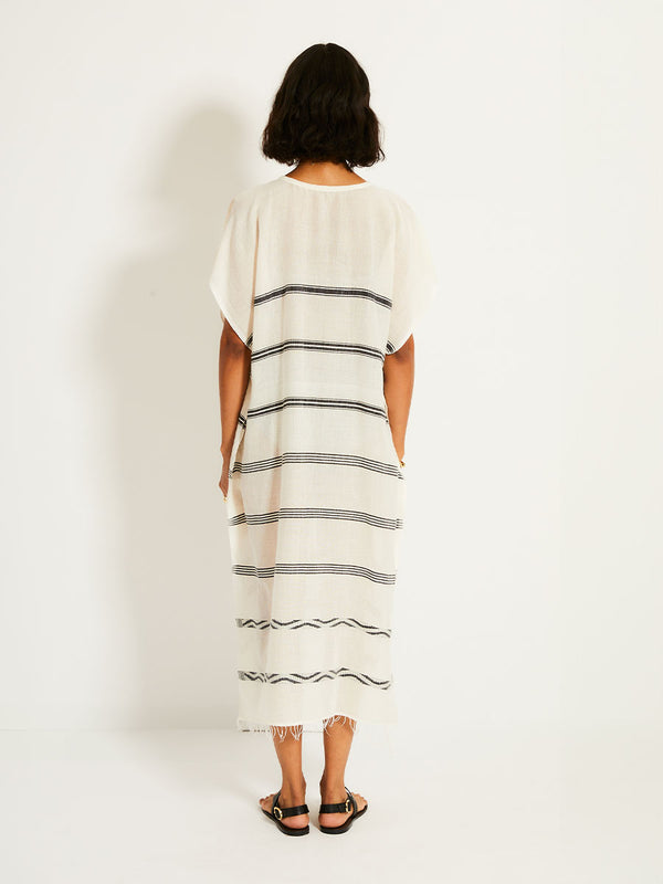 Back of a Woman Standing Wearing lemlem DALILA Caftan featuring  black intricate stripes and a Tibeb wave band on a soft vanilla ground
