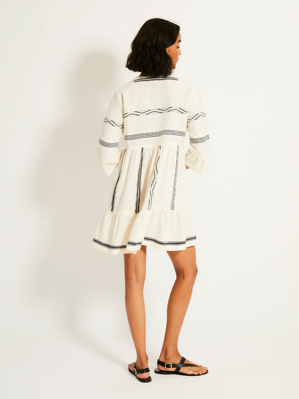 Back of a Woman Standing Wearing lemlem HANNA Flutter Dress featuring  black intricate stripes and a Tibeb wave band on a soft vanilla ground