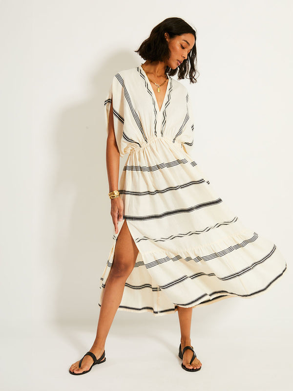 Woman Standing Wearing lemlem LEILA Dress featuring  black intricate stripes and a Tibeb wave band on a soft vanilla ground