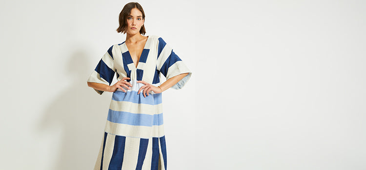 Woman Standing Wearing lemlem ENDA Dress featuring color block pattern in blue and cream colors