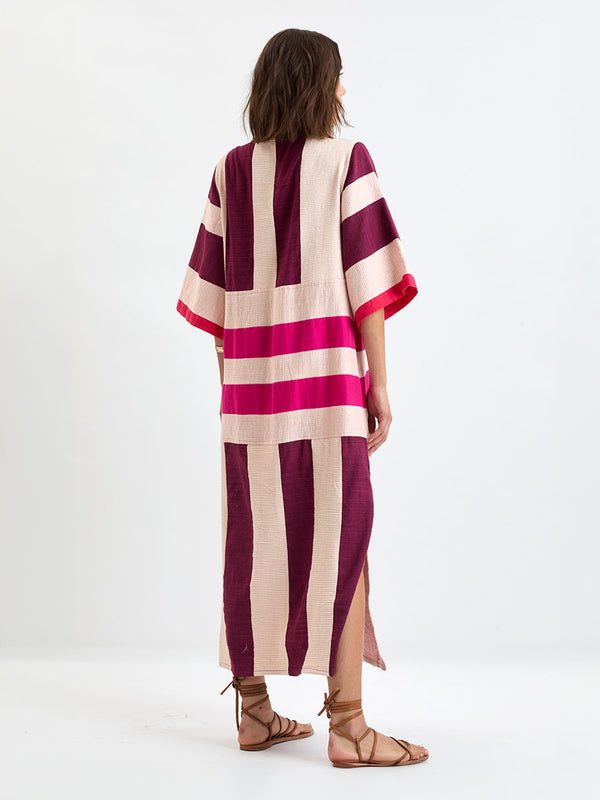 Back of a Woman standing wearing lemlem EDNA Dress  featuring a striking color-block combination of vivid magenta, scarlet, and burgundy colors.