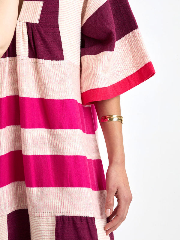 Close up on a Woman standing wearing lemlem EDNA Dress  featuring a striking color-block combination of vivid magenta, scarlet, and burgundy colors.