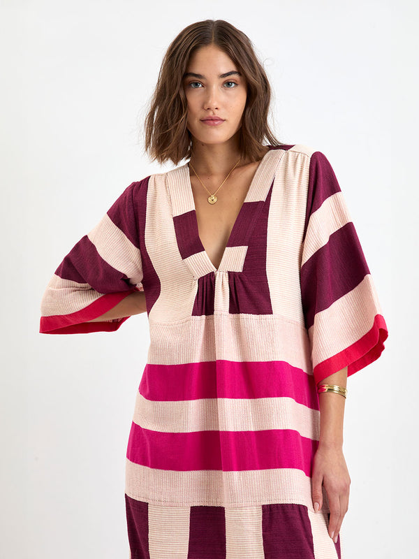Woman standing wearing lemlem EDNA Dress  featuring a striking color-block combination of vivid magenta, scarlet, and burgundy colors.