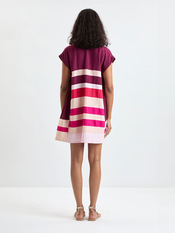 Back of a woman standing wearing lemlem ELINA Caftan featuring a striking color-block combination of vivid magenta, scarlet, and burgundy colors.
