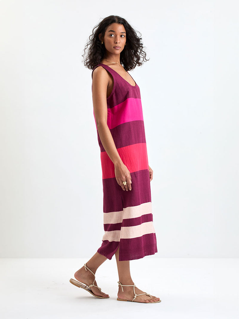 Side shot of a Woman standing wearing lemlem LILIAN Tank Dress featuring a striking color-block combination of vivid magenta, scarlet, and burgundy colors.