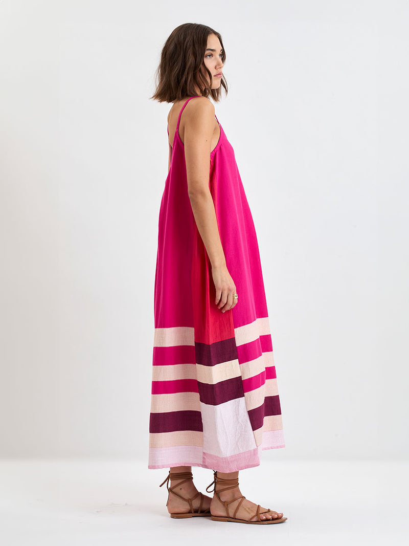 Side shot of a Woman standing wearing lemlem  NIA Slip Dress  featuring a striking color-block combination of vivid magenta, scarlet, and burgundy colors.