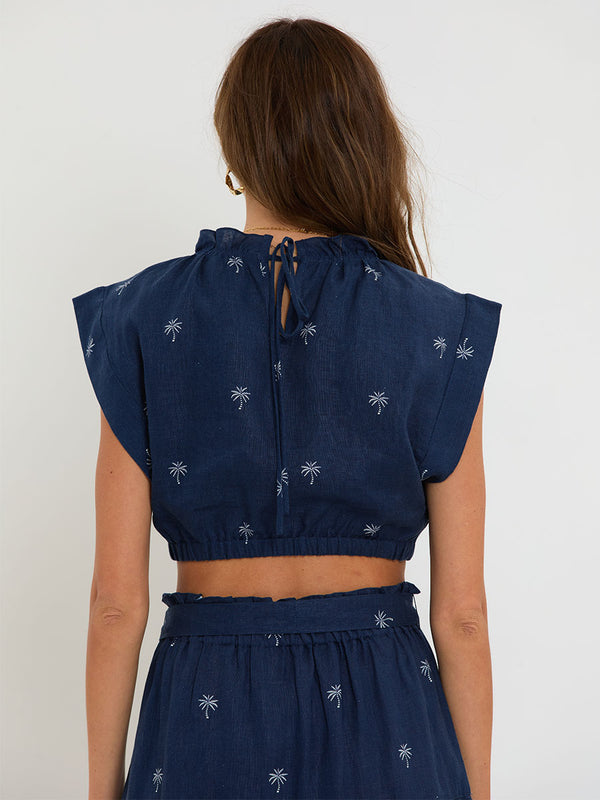 Woman Standing Wearing lemlem MUNA Top and SANAA Skirt featuring ivory palm tree motifs set against a rich navy background.