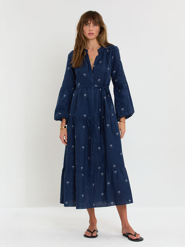 Woman Standing Wearing lemlem NESANET Peasant Dress featuring ivory palm tree motifs set against a rich navy background.