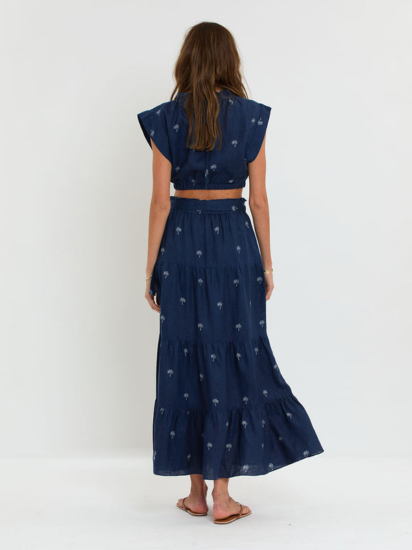 Woman Standing Wearing lemlem MUNA Top and SANAA Skirt featuring ivory palm tree motifs set against a rich navy background.