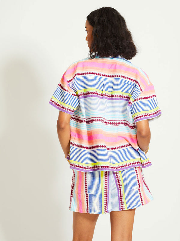 Back of a Woman Standing Wearing lemlem TUULI | Cabana Shirt featuring  intricate stripes in sun-washed hues and a Tibeb-inspired pattern in rich dark plum