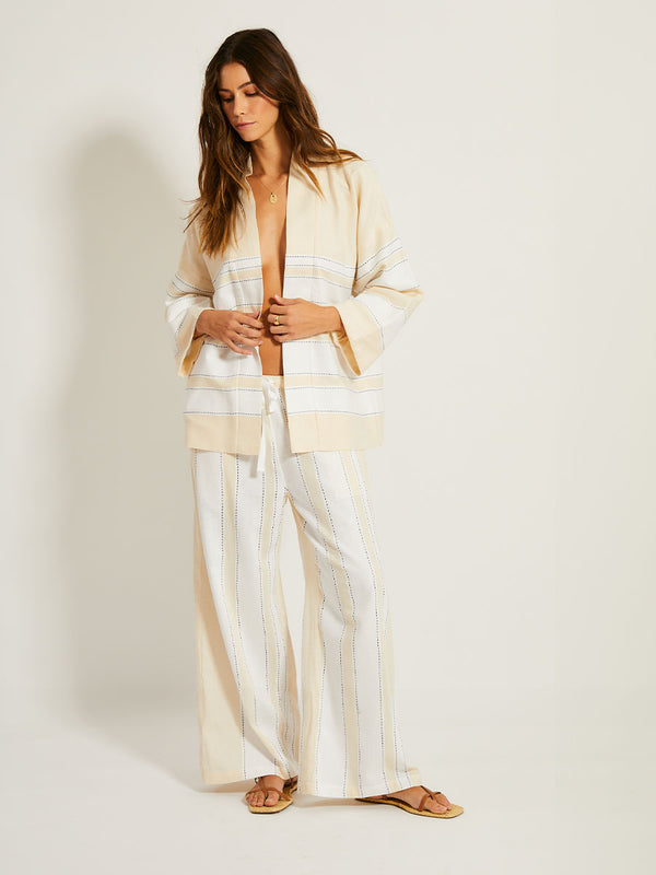 Woman Standing Wearing lemlem DESTA Pants featuring bold stripes in bright white on a vanilla cream background, accented with navy pick stitch detailing