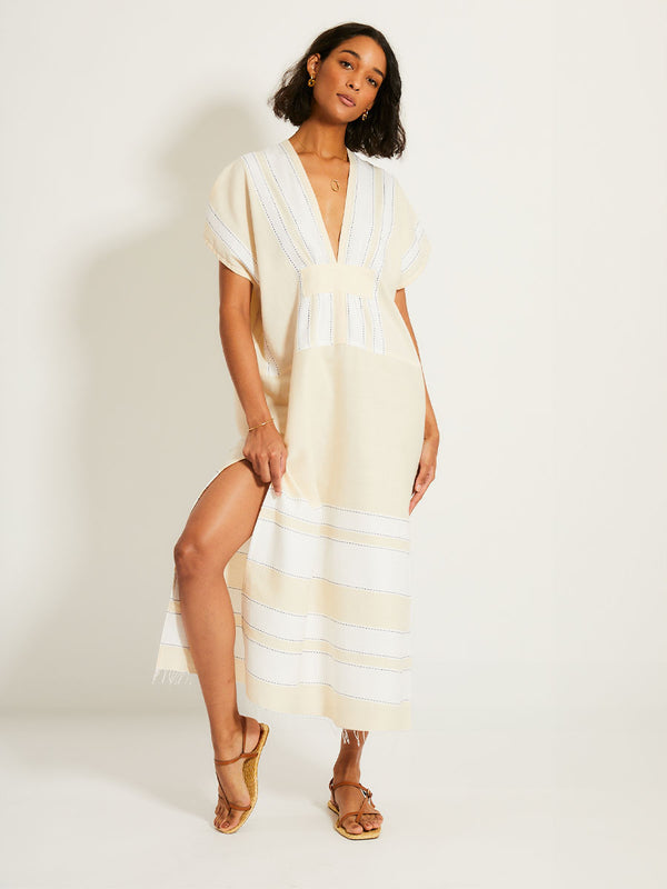 Woman Standing Wearing lemlem GASIRA Caftan featuring bold stripes in bright white on a vanilla cream background, accented with navy pick stitch detailing