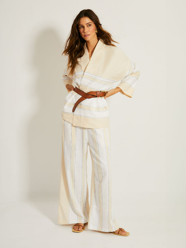 Woman Standing Wearing lemlem TERARA Jacket featuring bold stripes in bright white on a vanilla cream background, accented with navy pick stitch detailing