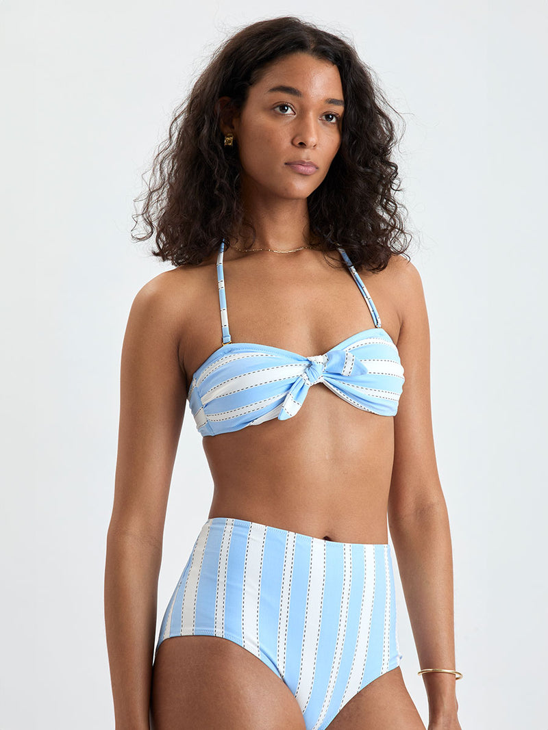 Woman wearing  lemlem ELSI High Waist bottom and AVA Bandeau Top featuring bold, crisp white stripes on a sky-blue background, accented with black detailing.