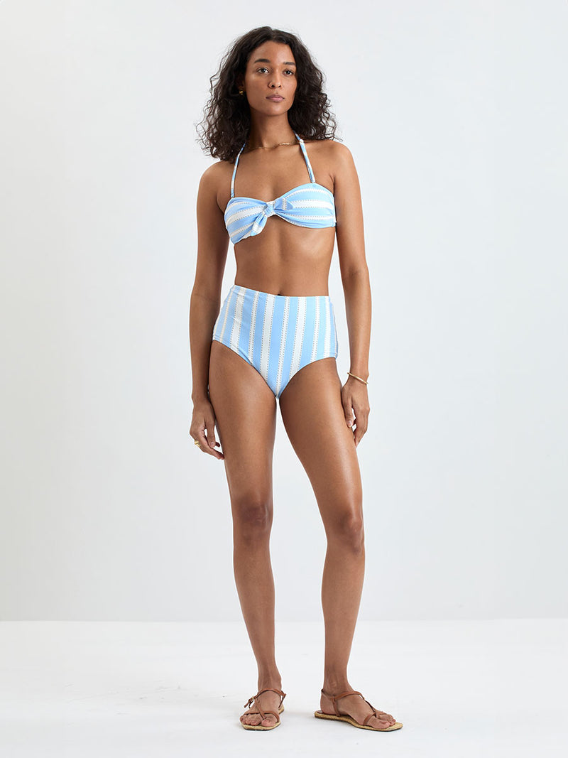 Woman wearing  lemlem ELSI High Waist bottom and AVA Bandeau Top featuring bold, crisp white stripes on a sky-blue background, accented with black detailing.