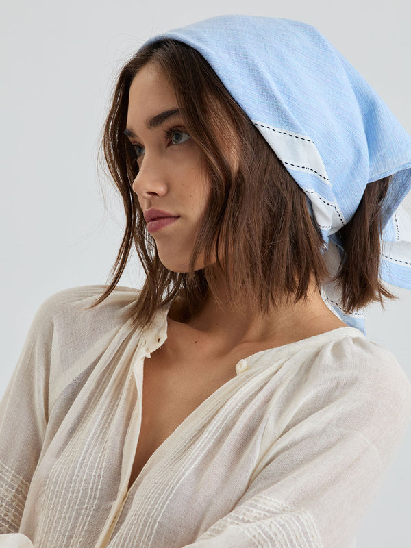 Woman standing wearing lemlem DANA Bandana featuring bold, crisp white stripes on a sky-blue background, accented with black detailing.