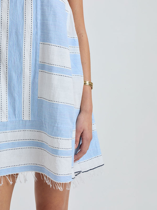 Close up on a Woman Standing wearing lemlem ELINA Caftan featuring bold, crisp white stripes on a sky-blue background, accented with black detailing.