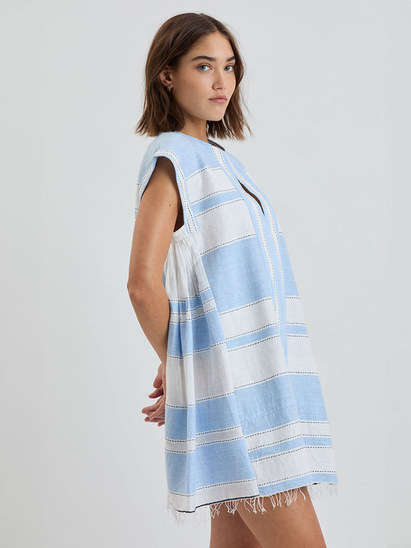 Woman Standing wearing lemlem ELINA Caftan featuring bold, crisp white stripes on a sky-blue background, accented with black detailing.