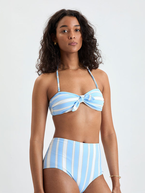 Woman wearing  lemlem ELSI High Waist bottom and AVA Bandeau Top featuring bold, crisp white stripes on a sky-blue background, accented with black detailing.